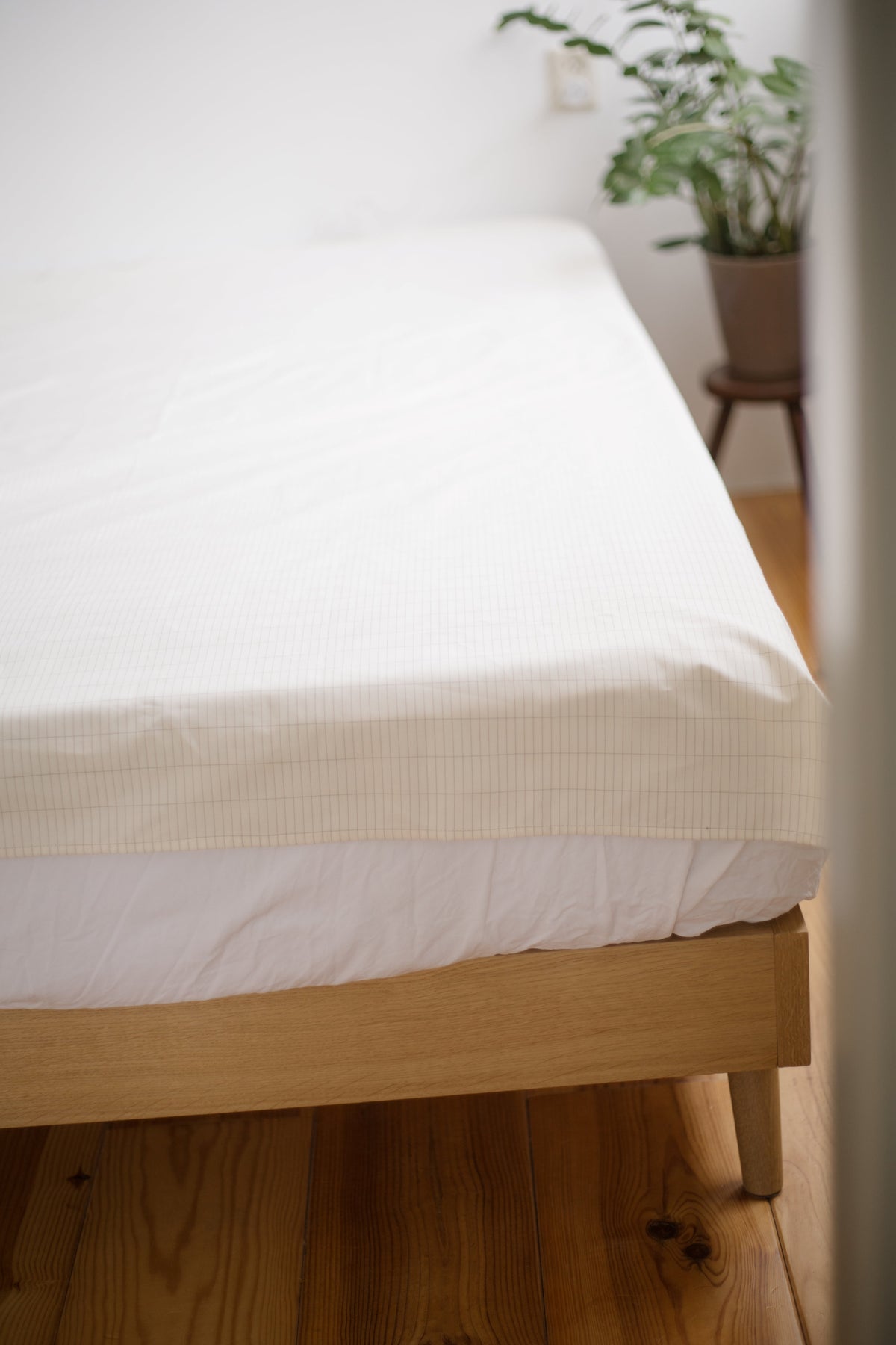 Earthle aardingslaken strak over het matras met een kamerplant op de achtergrond
