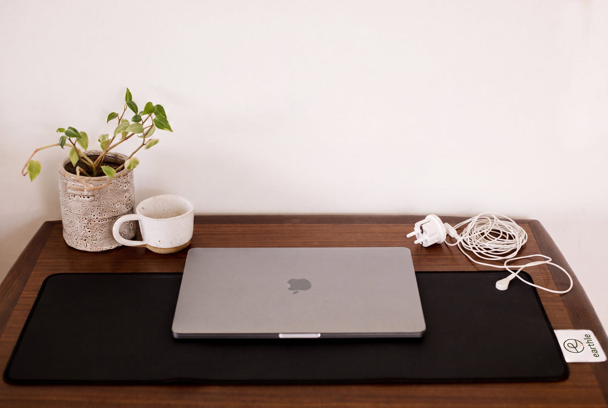 Earthle aardingsbureaumat op een bureau met laptop, plant en beker, kabel naar het stopcontact
